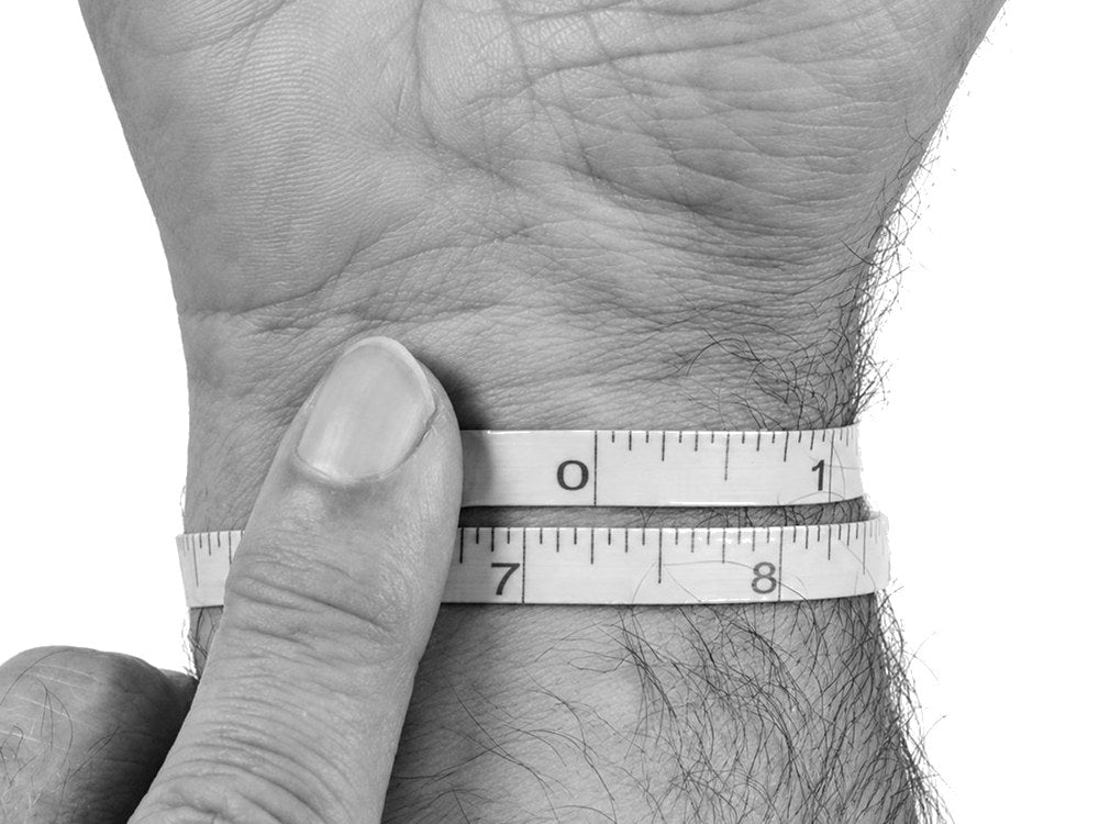 A soft tape measured around a wrist, snug against the skin; the end of the tape meets between the 7 and 8 inch marks, reading 7.25 inches